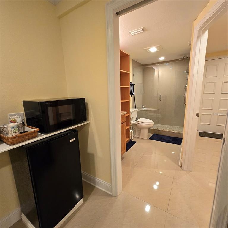 A small kitchenette area with a microwave and mini-fridge sits beside a tiled bathroom — 36750 US HIGHWAY 19 N UNIT 11-104, PALM HARBOR, FL