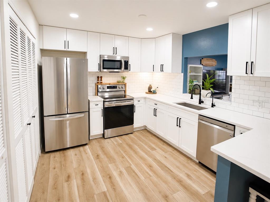 A kitchen with white cabinets, stainless steel appliances, white subway tile, and wood-look flooring — 2384 HOUNDS TRAIL, PALM HARBOR, FL