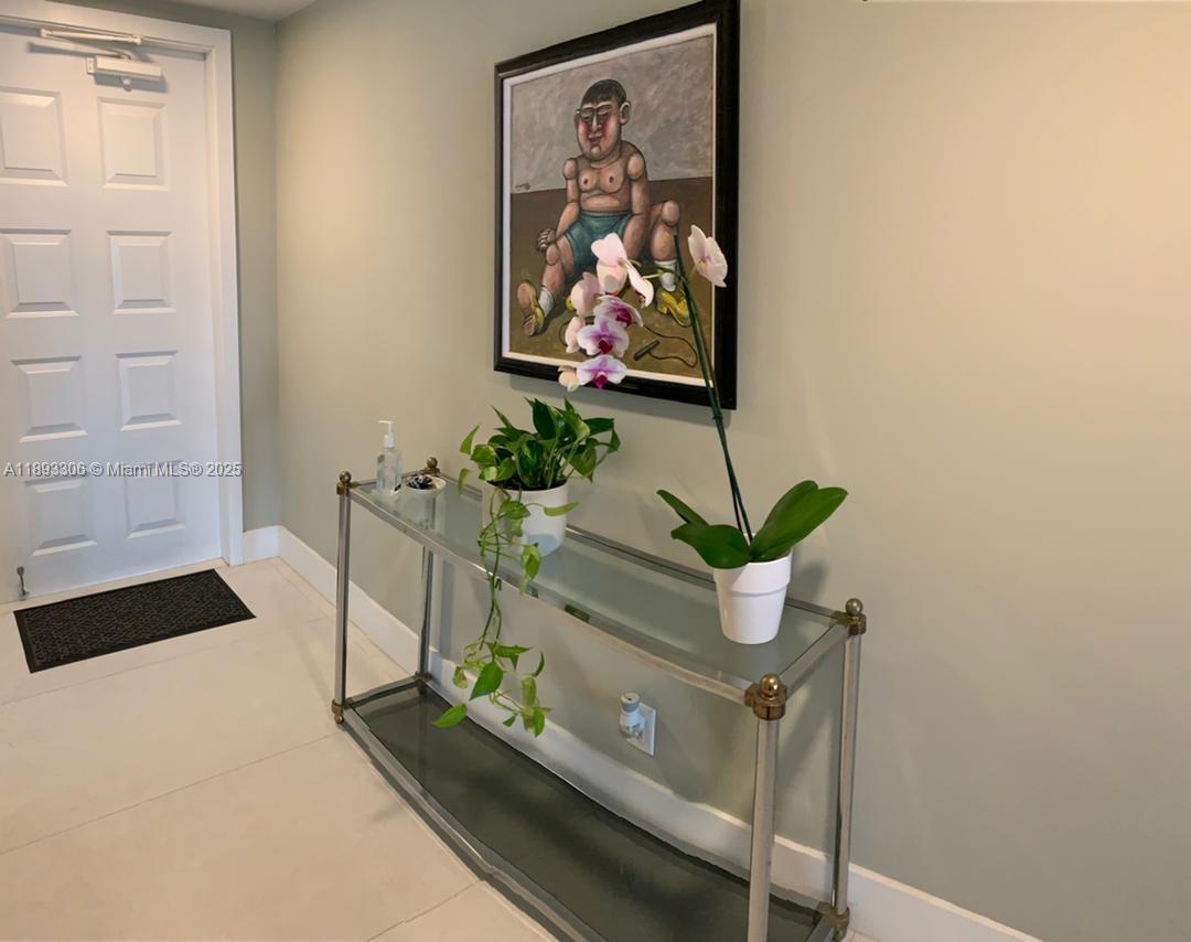 A glass console table with plants sits against a wall beneath a framed painting — 3507 Oaks Way # 802, Pompano Beach FL 33069, POMPANO BEACH, FL