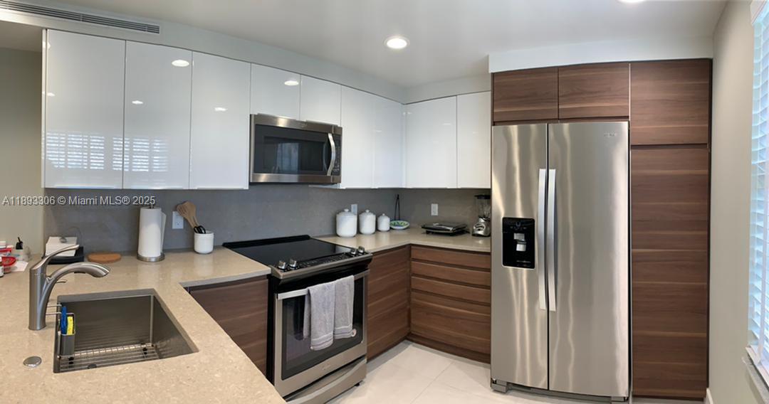 A modern kitchen features white upper cabinets, wood-toned lower cabinets, stainless steel appliances, and countertops — 3507 Oaks Way # 802, Pompano Beach FL 33069, POMPANO BEACH, FL