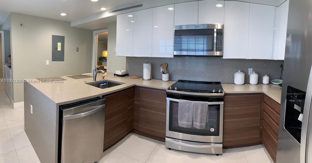 A modern kitchen features white upper cabinets, wood-toned lower cabinets, and stainless steel appliances — 3507 Oaks Way # 802, Pompano Beach FL 33069, POMPANO BEACH, FL