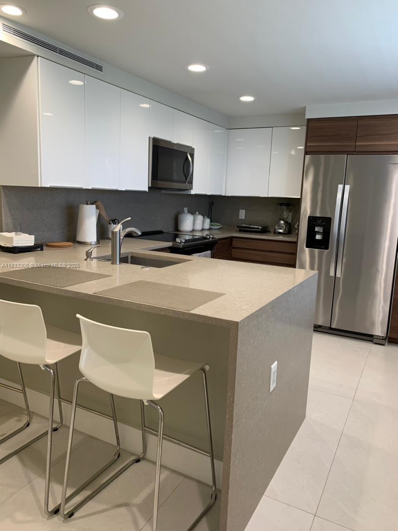 A modern kitchen features white upper cabinets, wood-tone lower cabinets, stainless steel appliances, and a peninsula — 3507 Oaks Way # 802, Pompano Beach FL 33069, POMPANO BEACH, FL