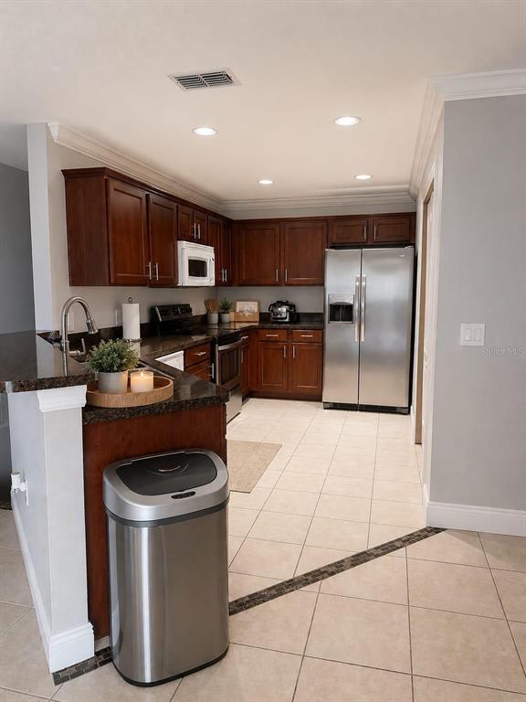 A kitchen features dark wood cabinets, stainless steel appliances, granite countertops, and light tile flooring — 3913 PEMBERLY, ST CLOUD, FL
