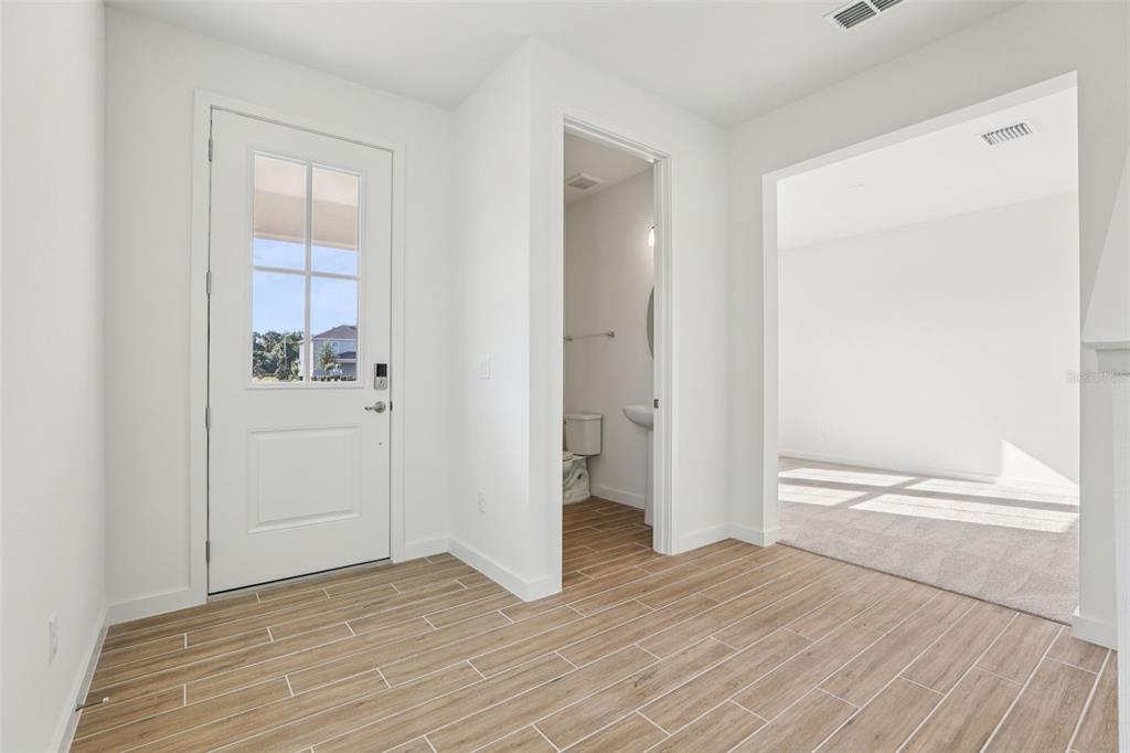 A bright entryway features wood-look tile flooring, a white door, and a small powder room — 1950 EDUCATION STREET, ST CLOUD, FL