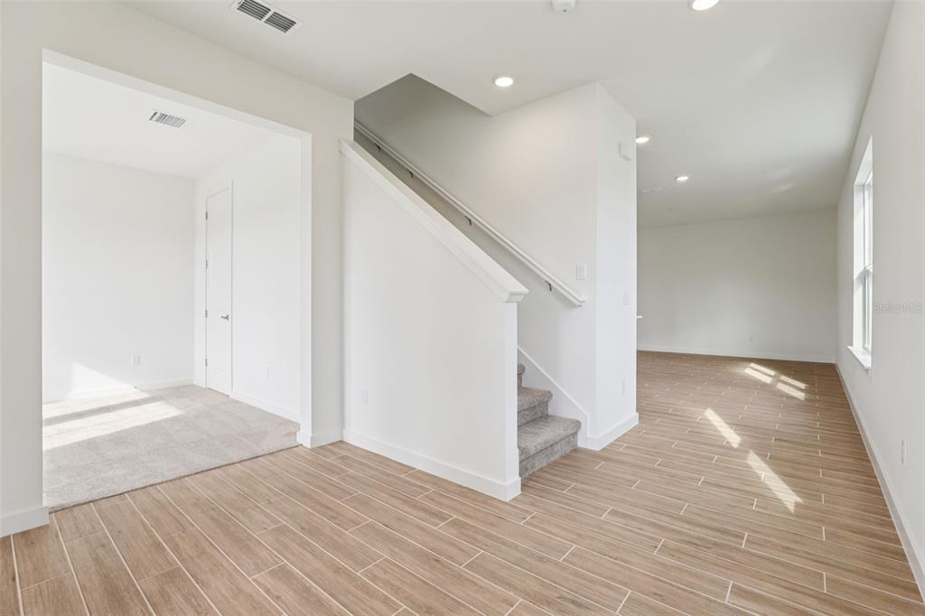 An interior view shows a staircase with carpeted steps, wood-look tile flooring, and white walls — 1950 EDUCATION STREET, ST CLOUD, FL