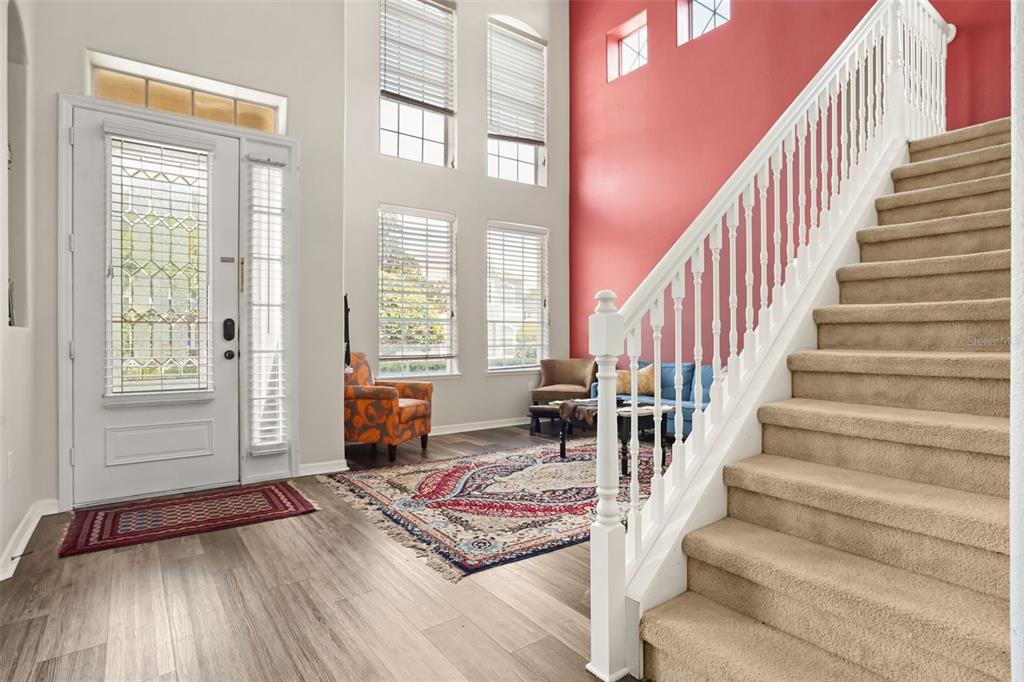 An entryway with a staircase, a red accent wall, and a patterned area rug — 1699 SWALLOWTAIL LANE, SANFORD, FL