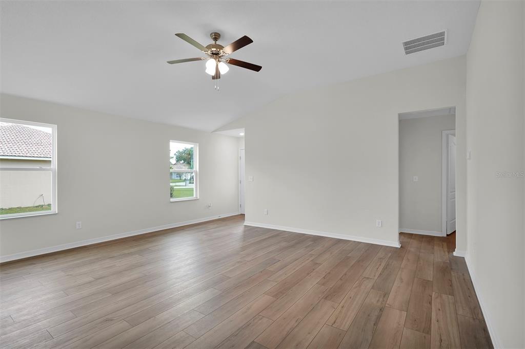 An empty living room features light-colored walls, wood-look flooring, a ceiling fan, and two windows — 616 MARION OAKS BOULEVARD, OCALA, FL