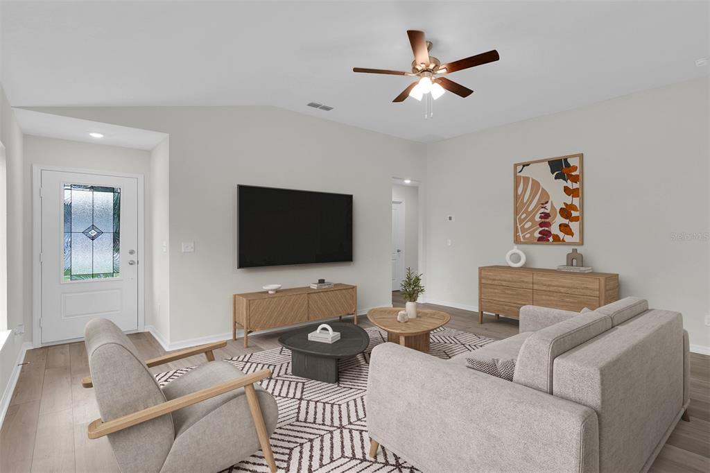 A living room features a vaulted ceiling, light wood flooring, a television, and neutral furniture — 616 MARION OAKS BOULEVARD, OCALA, FL