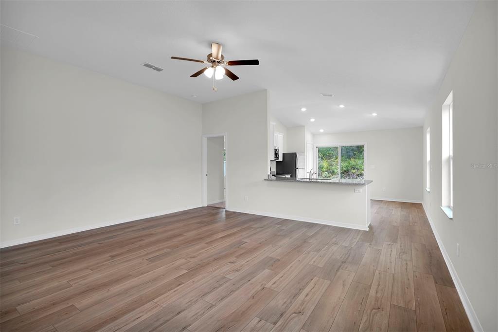 An open-concept living room with wood-look flooring, a ceiling fan, and a kitchen pass-through — 616 MARION OAKS BOULEVARD, OCALA, FL