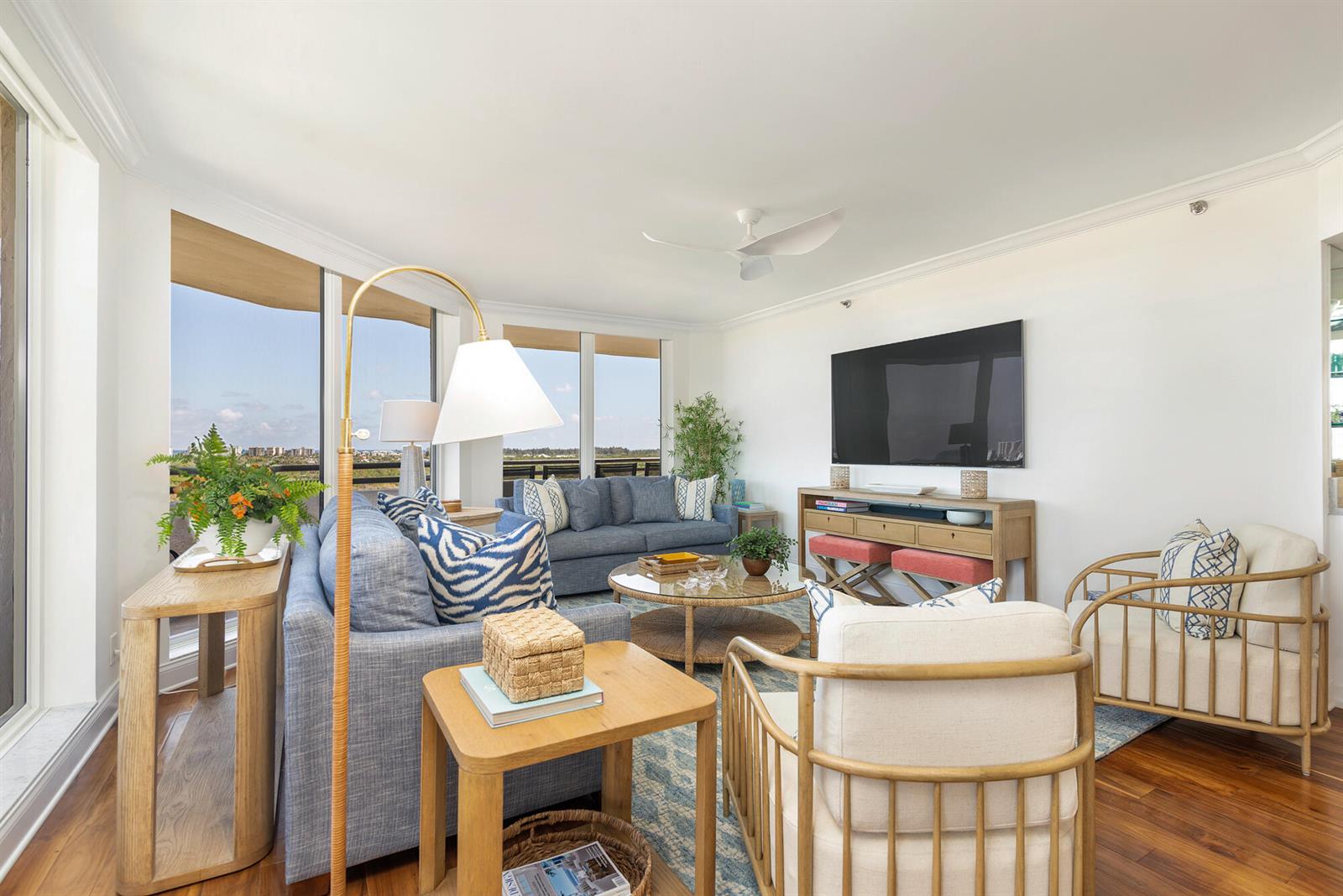 A living room features blue sofas, light wood furniture, a television, and floor-to-ceiling windows — 3322 Casseekey Island Road # 902, Jupiter FL 33477, JUPITER, FL