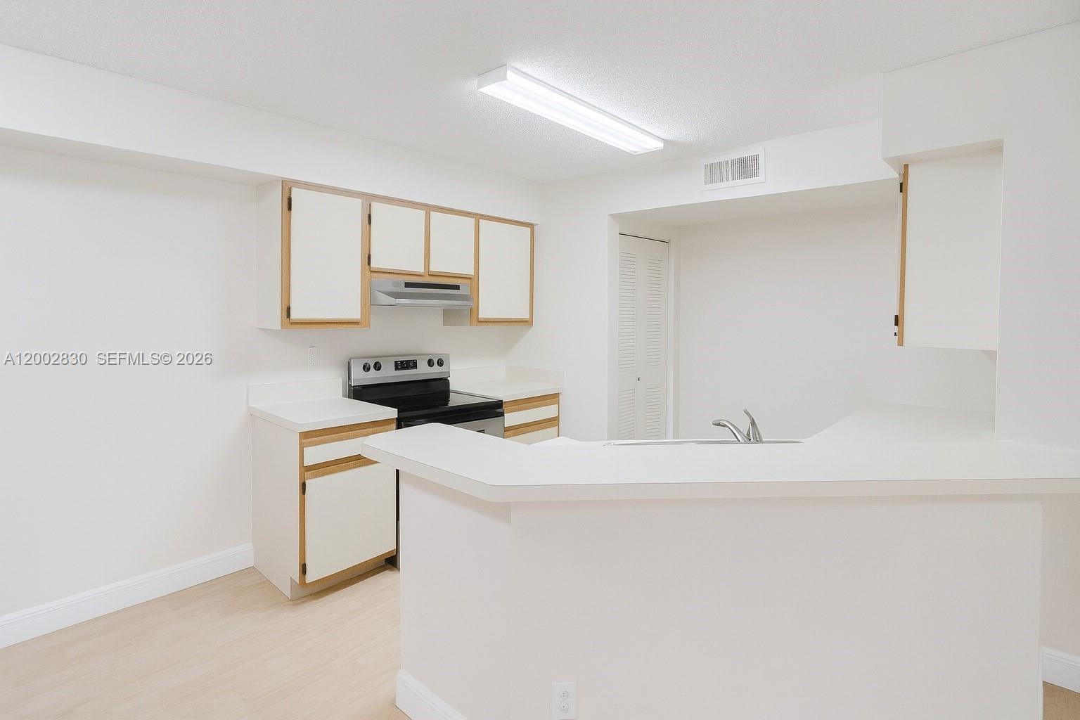 A kitchen features white cabinets with wood trim, white countertops, and a breakfast bar — 9999 Summerbreeze Dr # 216, Sunrise FL 33322, SUNRISE, FL