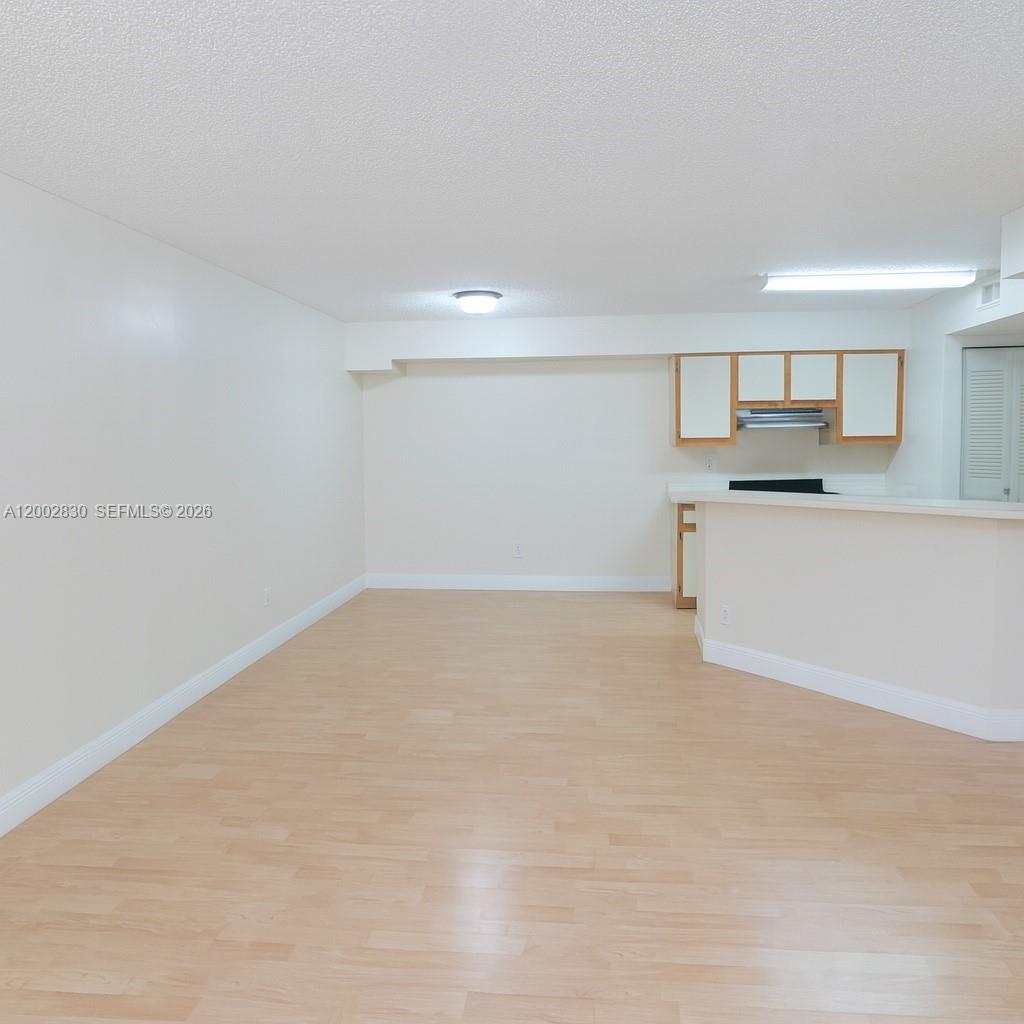 An empty room with light wood-look flooring features a kitchen pass-through counter and cabinets — 9999 Summerbreeze Dr # 216, Sunrise FL 33322, SUNRISE, FL
