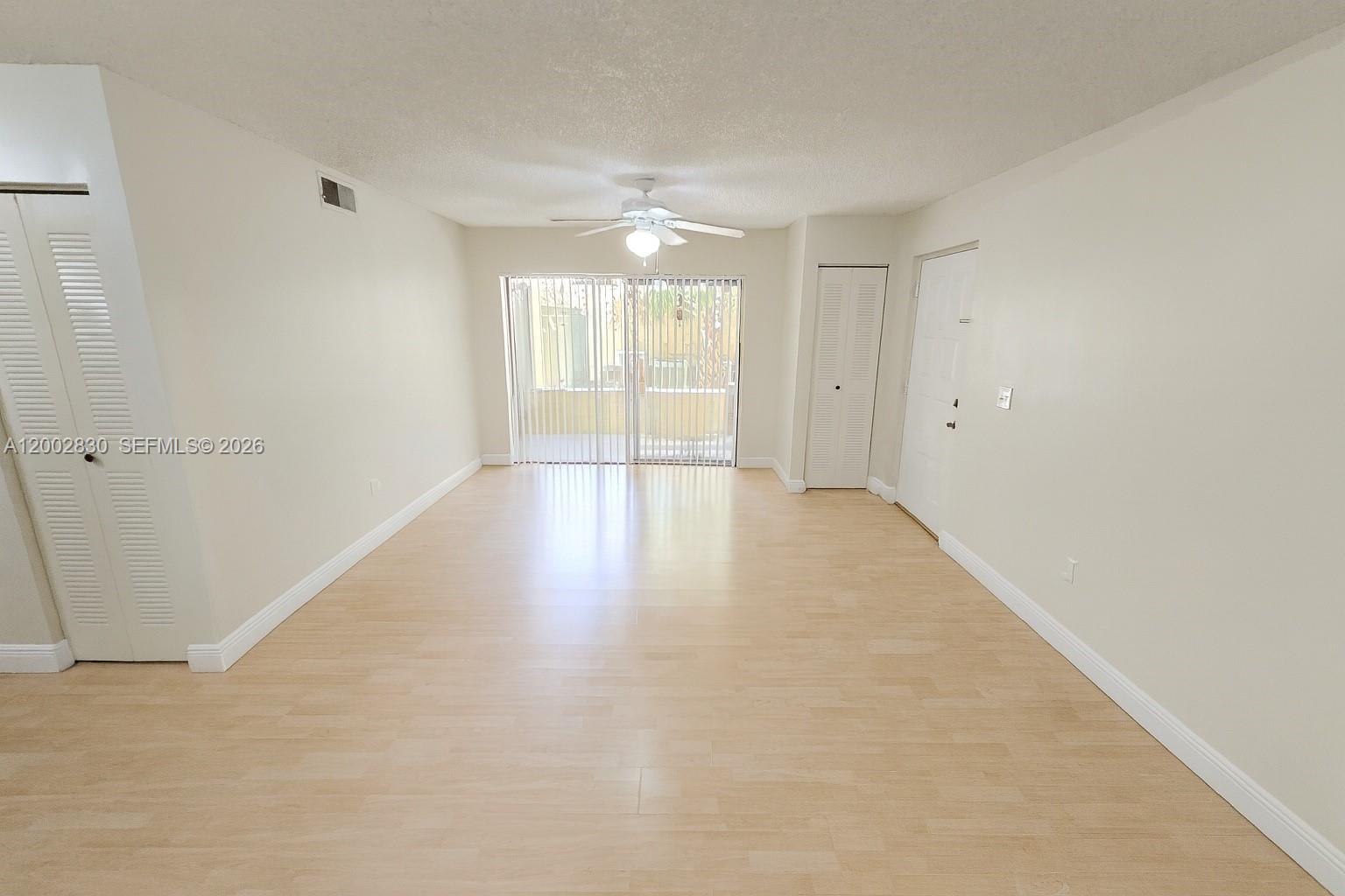 An empty living room features light-colored wood flooring, white walls, a ceiling fan, and sliding doors — 9999 Summerbreeze Dr # 216, Sunrise FL 33322, SUNRISE, FL