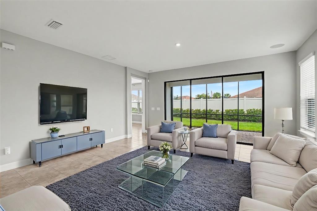 A living room features a blue media console, a glass coffee table, and sliding glass doors — 10930 WENDOVER DRIVE, PALMETTO, FL