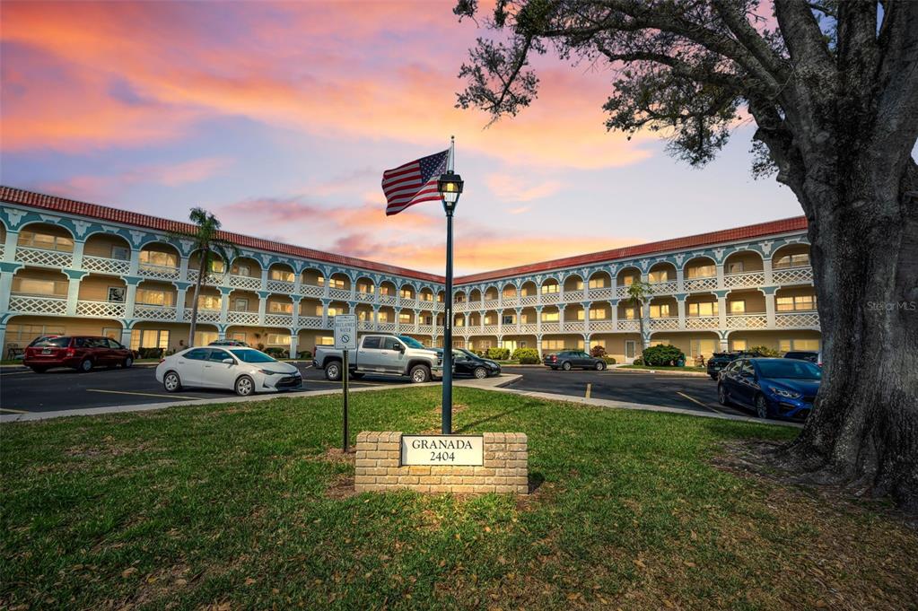 An exterior view of a multi-story apartment complex with a parking lot and flag pole — 2404 FLORENTINE WAY UNIT 20, CLEARWATER, FL