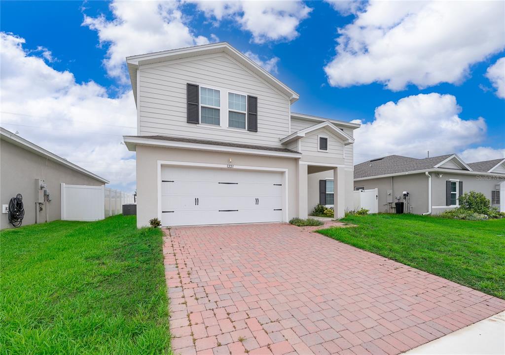 A two-story suburban house features a white garage, light siding, and a brick paver driveway — 1221 LEXINGTON LANE, HAINES CITY, FL