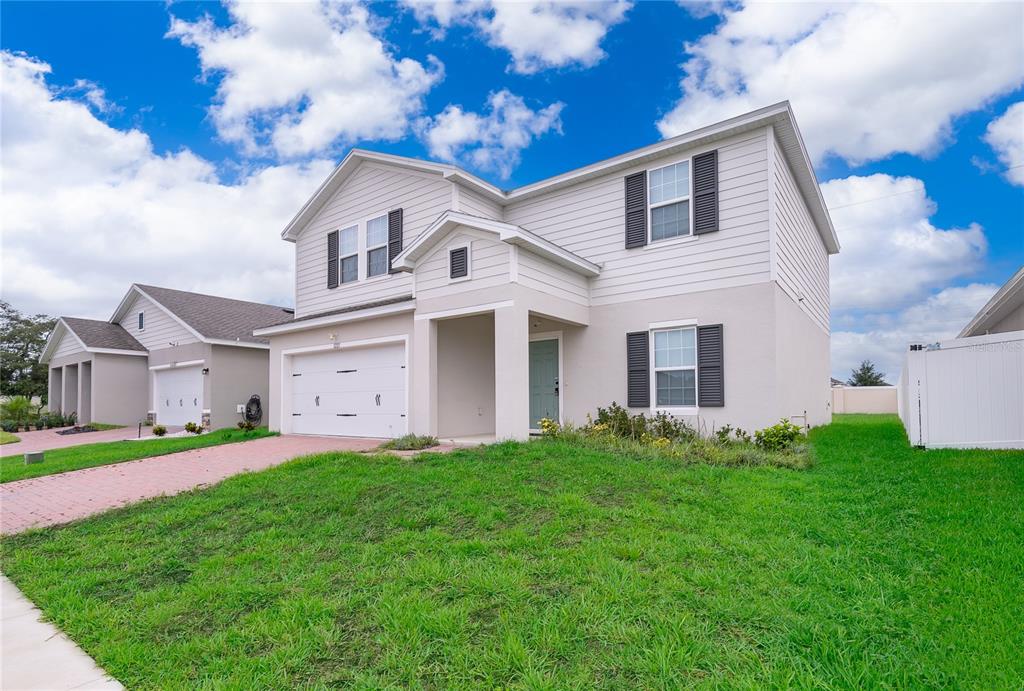 A two-story house with light-colored siding, a two-car garage, and a grassy front yard — 1221 LEXINGTON LANE, HAINES CITY, FL