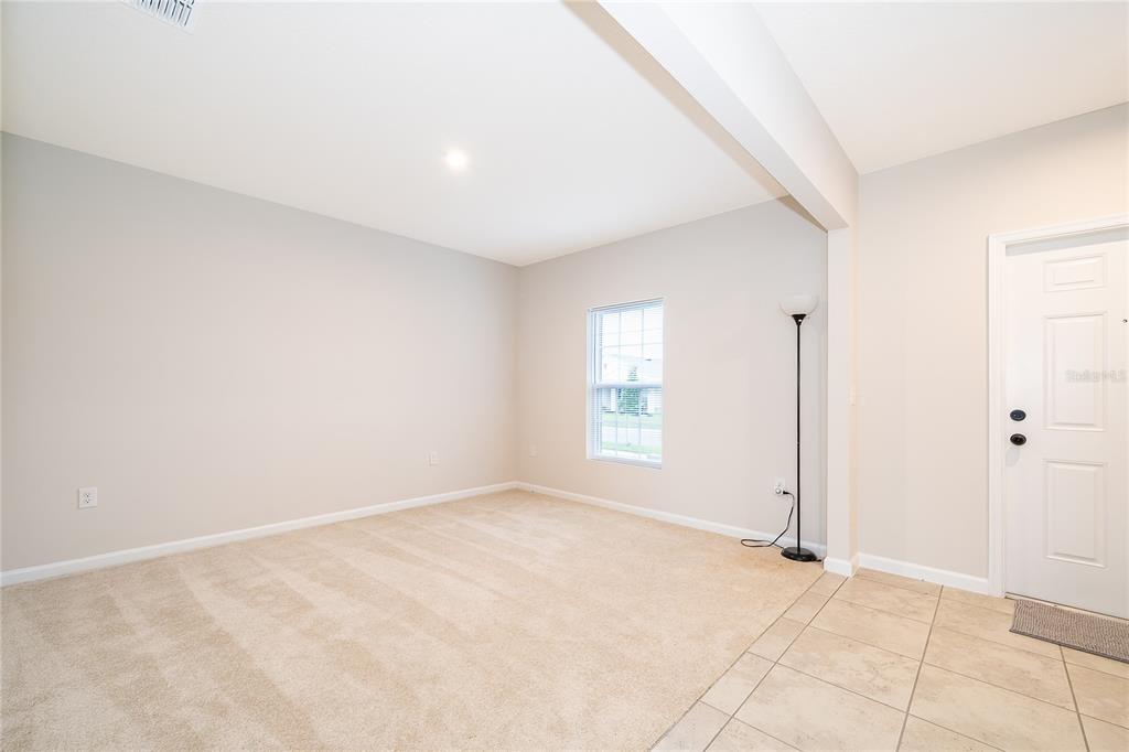 A living room features beige carpeting, light gray walls, a window, and a tile entryway — 1221 LEXINGTON LANE, HAINES CITY, FL