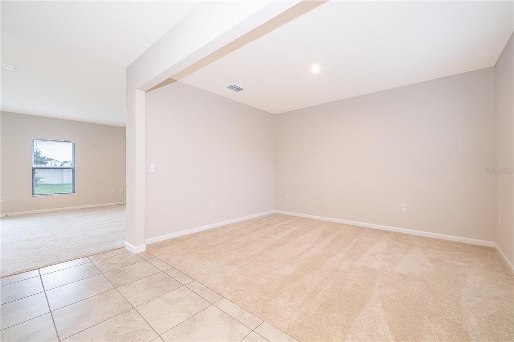 A carpeted room with beige walls connects to an adjacent carpeted living area — 1221 LEXINGTON LANE, HAINES CITY, FL