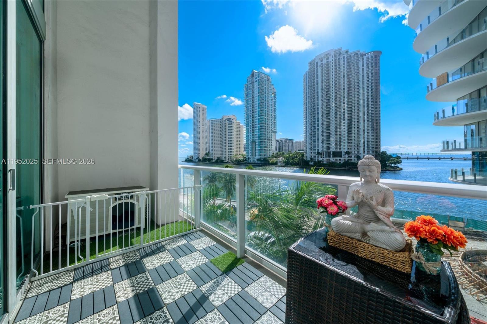 A balcony features patterned tile flooring, a white safety gate, and a Buddha statue overlooking water — 300 S BISCAYNE BLVD # 410, Miami FL 33131, MIAMI, FL