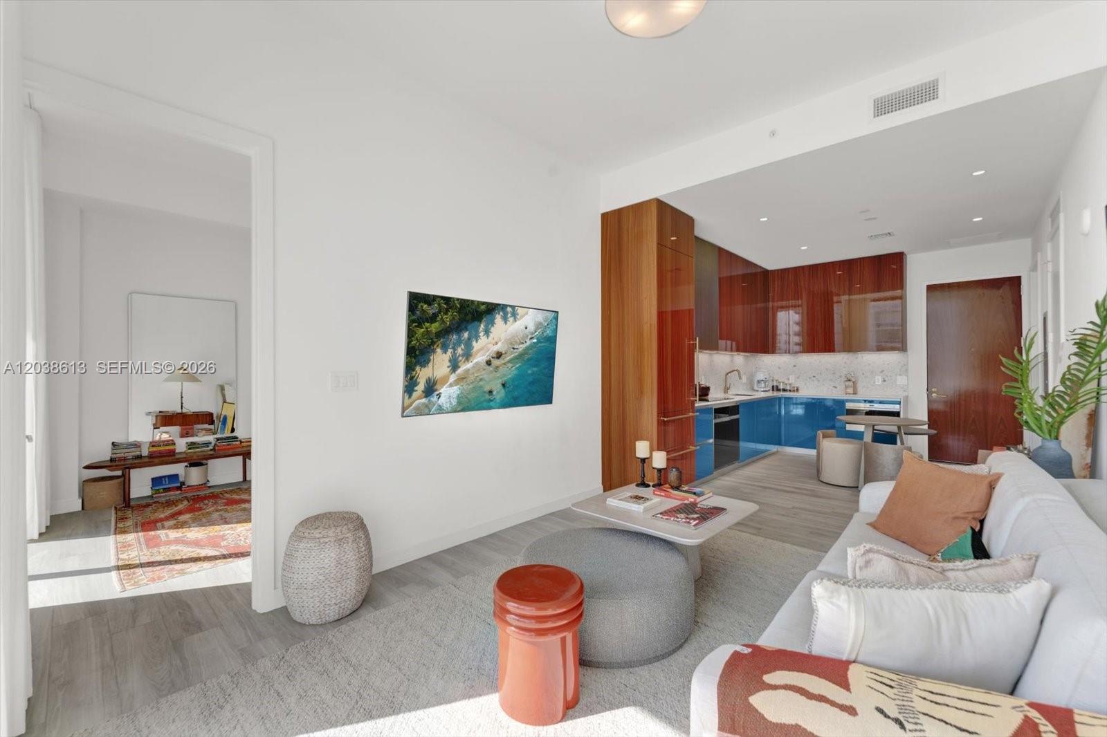 A living room with a wall-mounted television, a grey sofa, and an adjacent kitchen — 2655 S Bayshore Dr # 1606, Miami FL 33133, MIAMI, FL