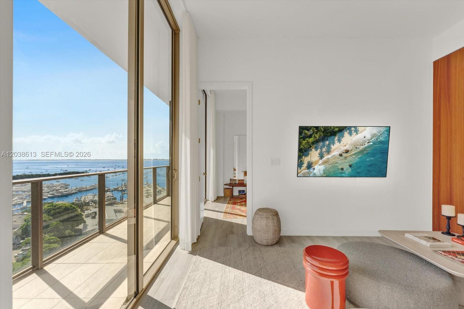 A bright room features a balcony with water views, a wall-mounted television, and wood flooring — 2655 S Bayshore Dr # 1606, Miami FL 33133, MIAMI, FL
