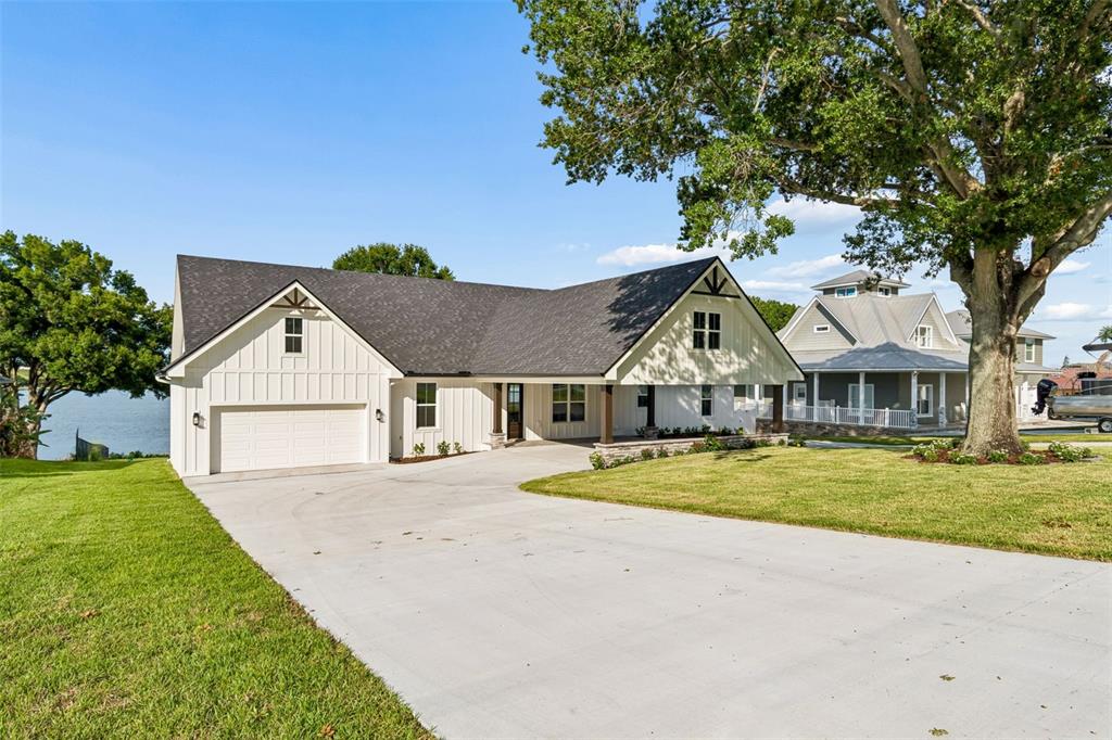A white farmhouse-style house with a dark roof and a concrete driveway sits near water — 5683 OLD BERKLEY ROAD, AUBURNDALE, FL
