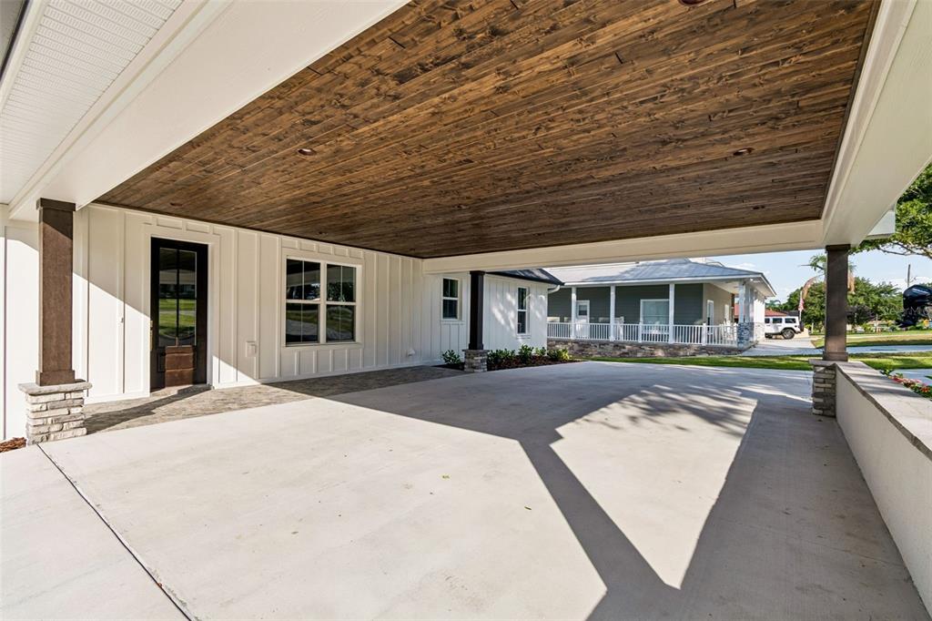 A covered concrete carport features a dark wood-paneled ceiling and white board-and-batten siding — 5683 OLD BERKLEY ROAD, AUBURNDALE, FL