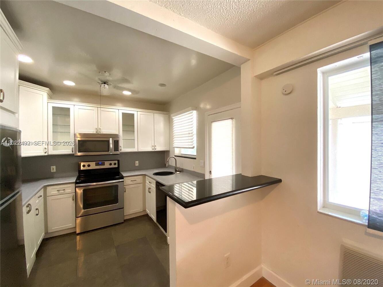 A kitchen features white cabinetry, stainless steel appliances, and a black countertop breakfast bar — 30 Park Dr # 16, Bal Harbour FL 33154, BAL HARBOUR, FL