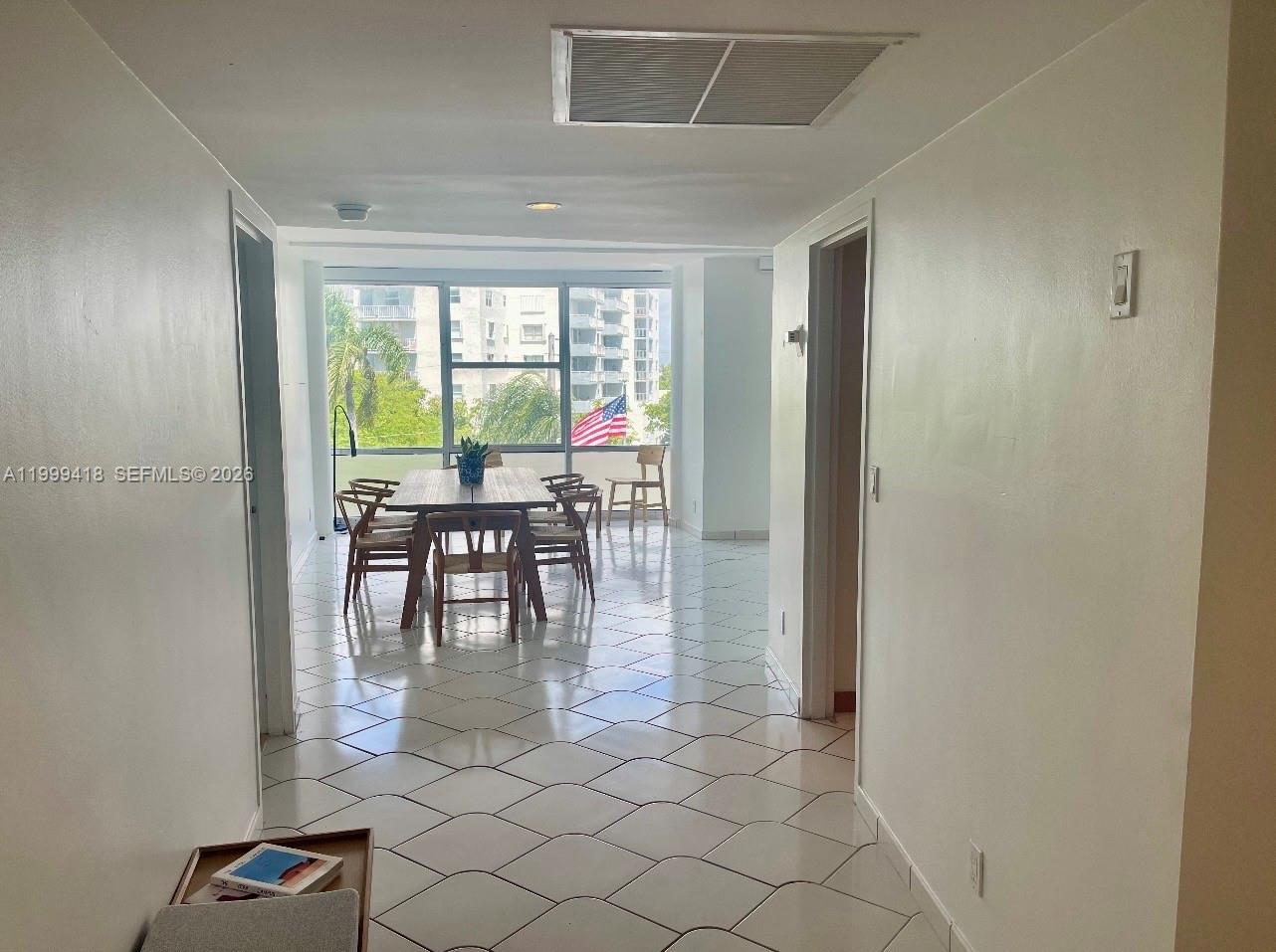 A dining area with a wooden table and chairs sits before large windows overlooking trees — 900 Bay Dr # 311, Miami Beach FL 33141, MIAMI BEACH, FL