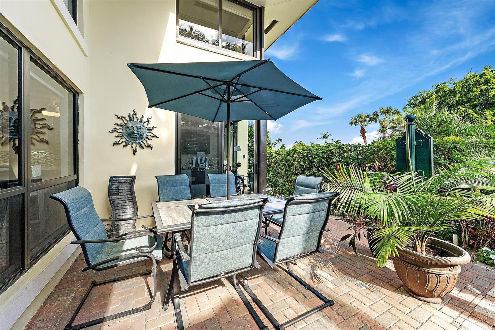 A patio with a dining set, umbrella, and potted palm sits beside a house exterior — 3693 Quail Ridge Drive # B, Boynton Beach FL 33436, BOYNTON BEACH, FL