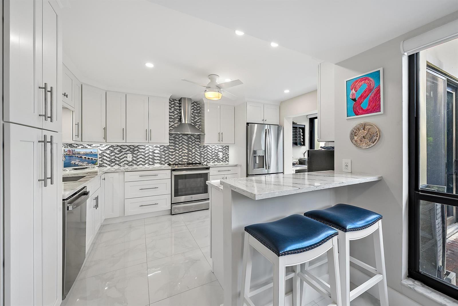 A modern kitchen features white cabinets, stainless steel appliances, a mosaic backsplash, and a breakfast bar — 3693 Quail Ridge Drive # B, Boynton Beach FL 33436, BOYNTON BEACH, FL