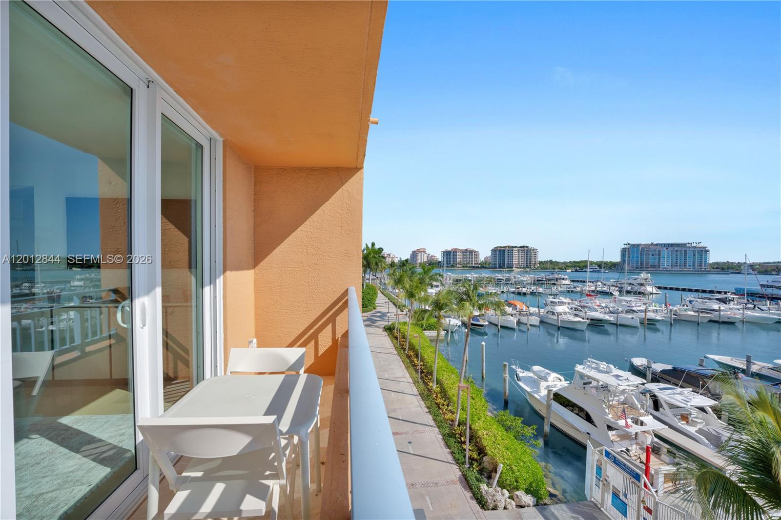 A balcony with a table and chairs overlooks a marina with numerous docked boats — 90 Alton Rd # 3, Miami Beach FL 33139, MIAMI BEACH, FL