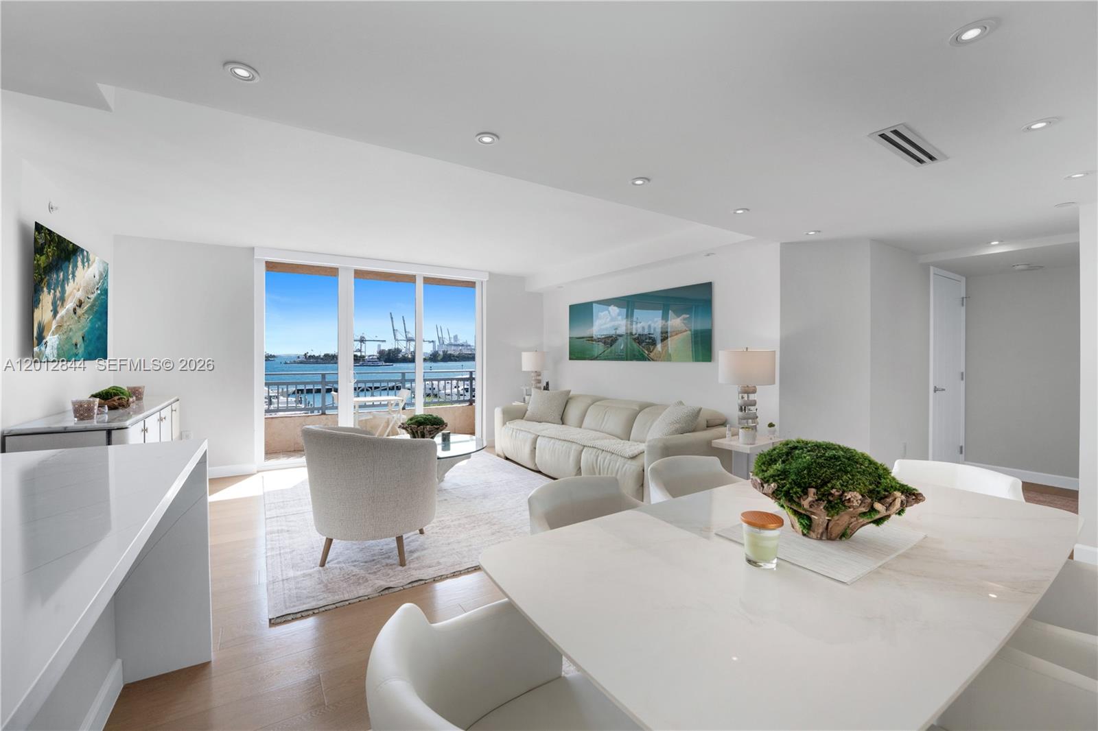A bright, open-concept living and dining area features white furniture, hardwood floors, and balcony views — 90 Alton Rd # 3, Miami Beach FL 33139, MIAMI BEACH, FL