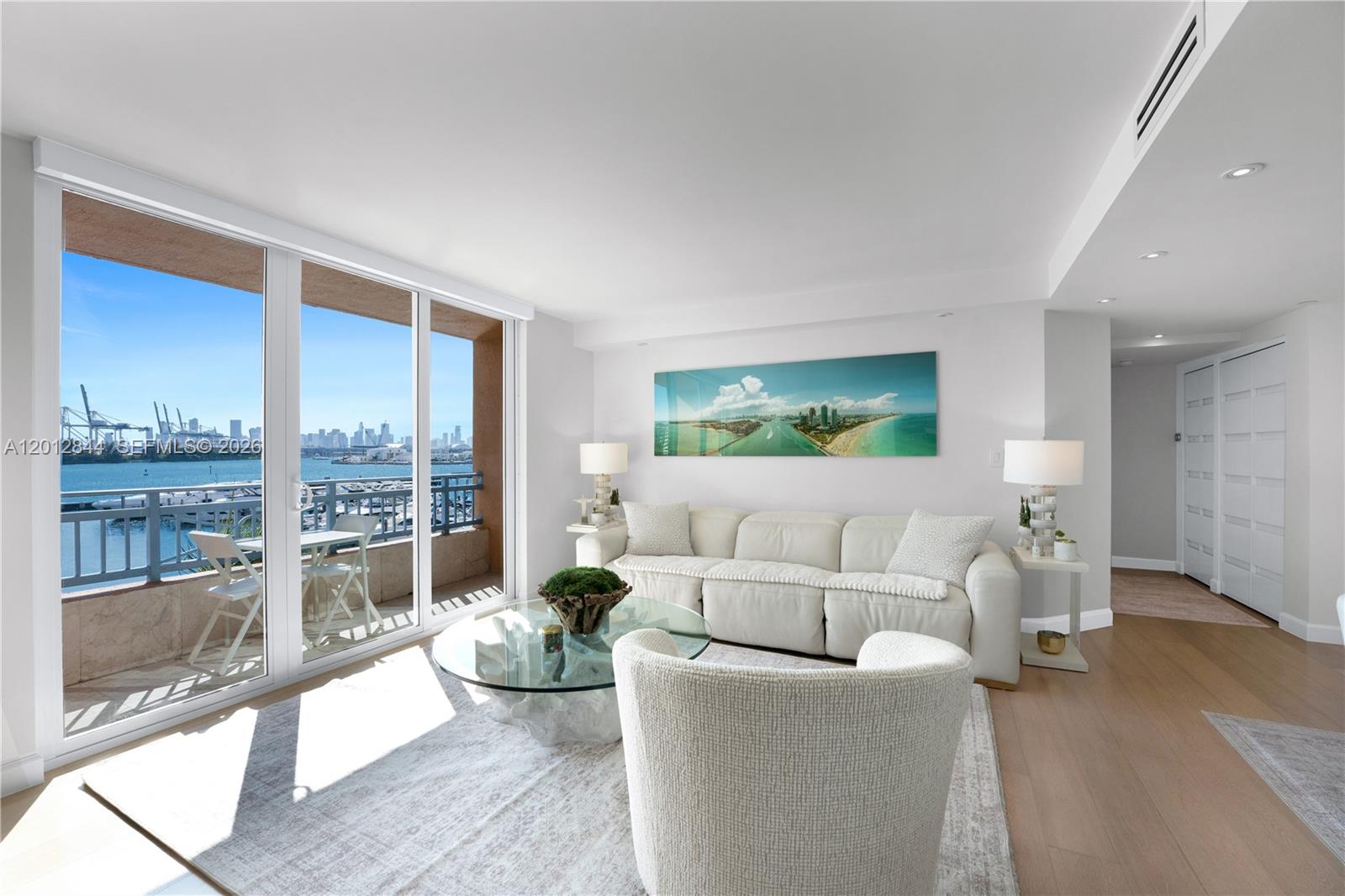 A bright living room features a white sofa, glass coffee table, and a balcony overlooking water — 90 Alton Rd # 3, Miami Beach FL 33139, MIAMI BEACH, FL