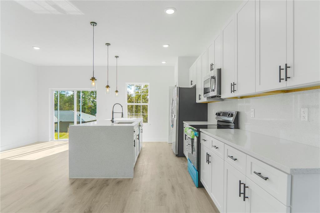 A modern kitchen features white cabinets, quartz countertops, a central island, and light wood flooring — 2632 SW 162ND STREET ROAD, OCALA, FL
