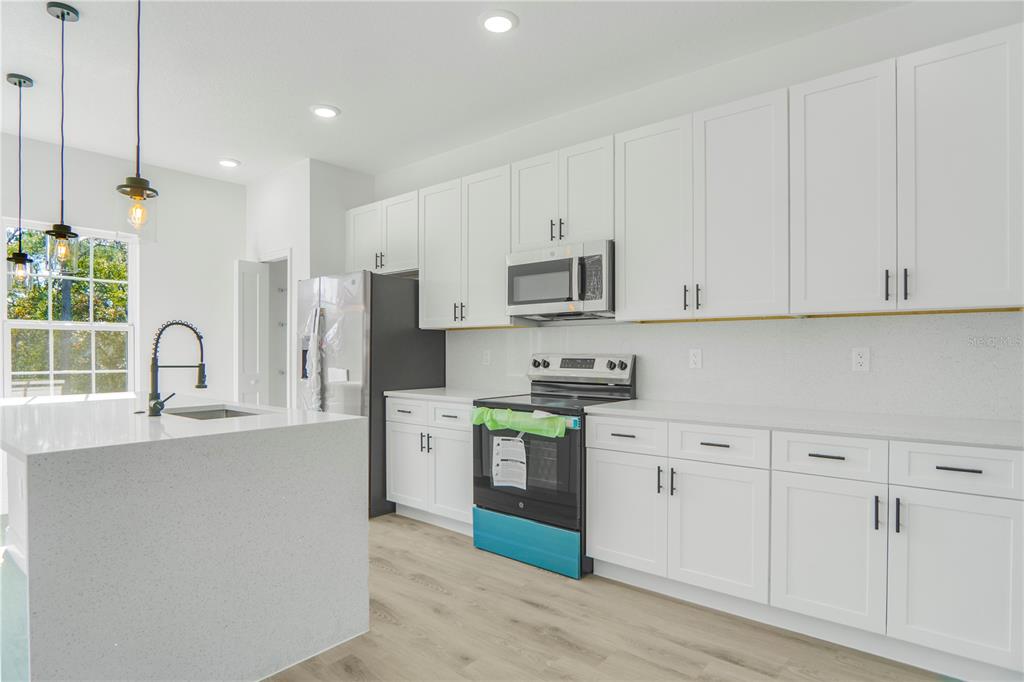 A modern kitchen features white cabinets, stainless steel appliances, a quartz island, and light flooring — 2632 SW 162ND STREET ROAD, OCALA, FL