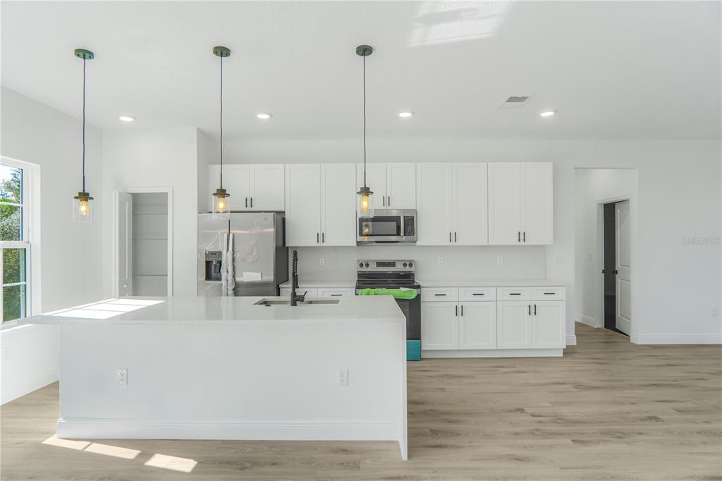 A modern kitchen features white cabinetry, a large island, stainless steel appliances, and wood flooring — 2632 SW 162ND STREET ROAD, OCALA, FL