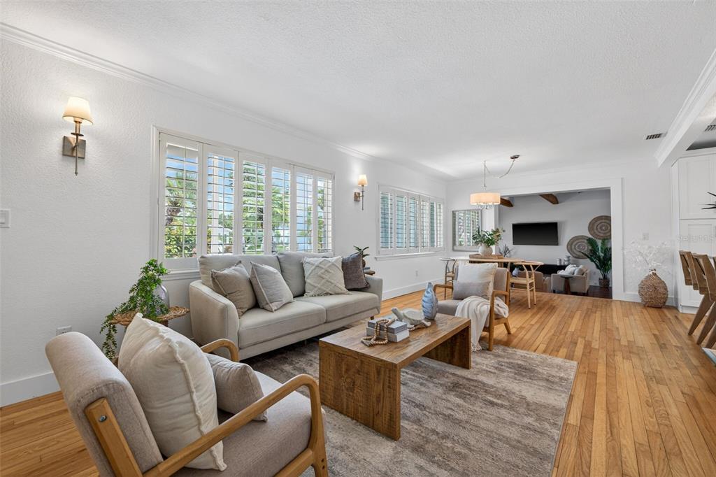 A bright living room features hardwood floors, a light gray sofa, and plantation shutters — 976 NARCISSUS AVENUE, CLEARWATER BEACH, FL