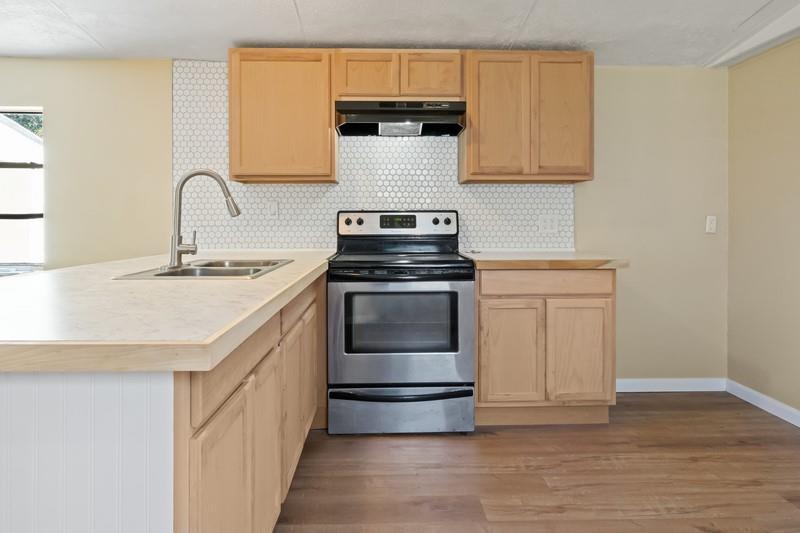 A kitchen features light wood cabinets, a stainless steel stove, and a white tiled backsplash — MERRITT ISLAND, FL