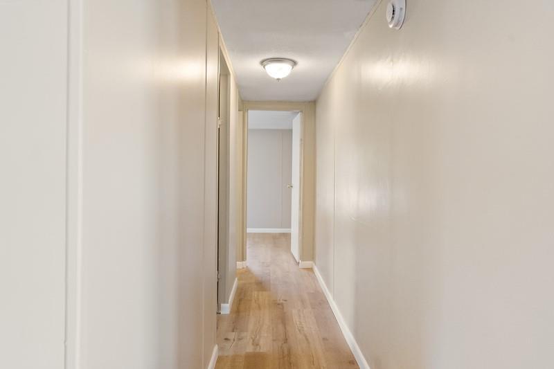 A narrow hallway with light-colored walls and wood-look flooring leads to an open doorway — MERRITT ISLAND, FL
