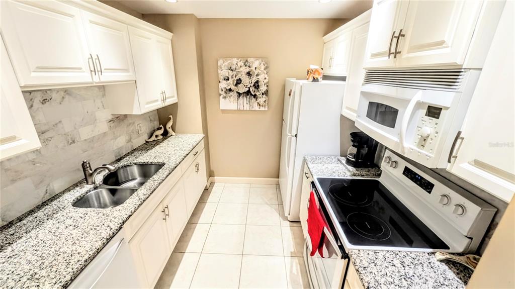 A galley kitchen features white cabinets, granite countertops, a double sink, and stainless steel appliances — 750 N TAMIAMI TRAIL UNIT 1404, SARASOTA, FL