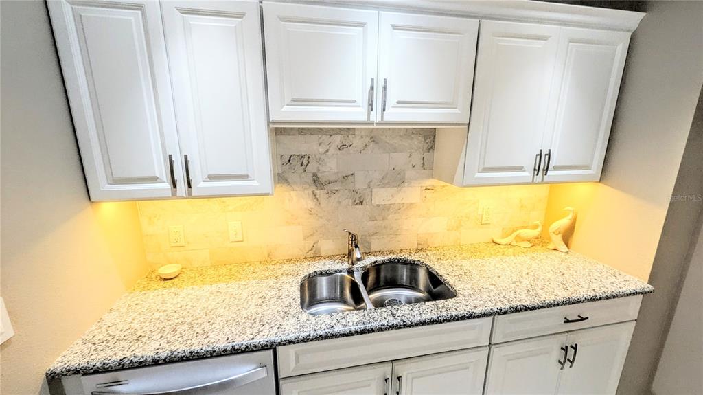A kitchen features white cabinets, a granite countertop, a stainless steel sink, and marble backsplash — 750 N TAMIAMI TRAIL UNIT 1404, SARASOTA, FL