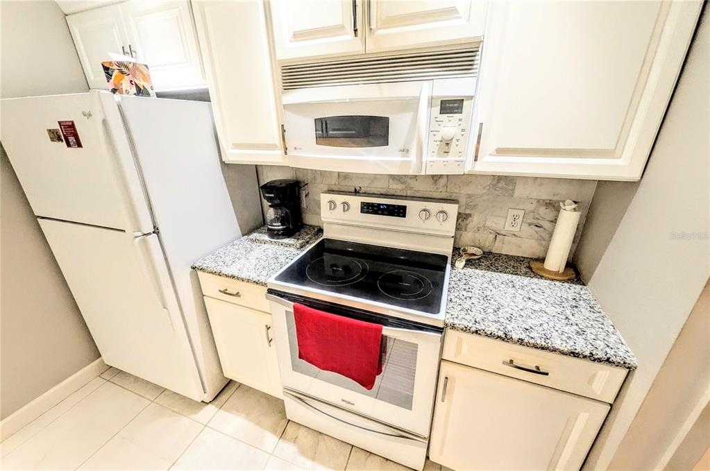 A kitchen features white cabinets, granite countertops, a white refrigerator, and a white electric range — 750 N TAMIAMI TRAIL UNIT 1404, SARASOTA, FL