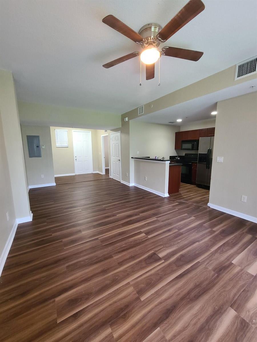 An open-concept living area features wood-look flooring, a ceiling fan, and an adjacent kitchen — 1955 Freeport Drive, Riviera Beach FL 33404, RIVIERA BEACH, FL