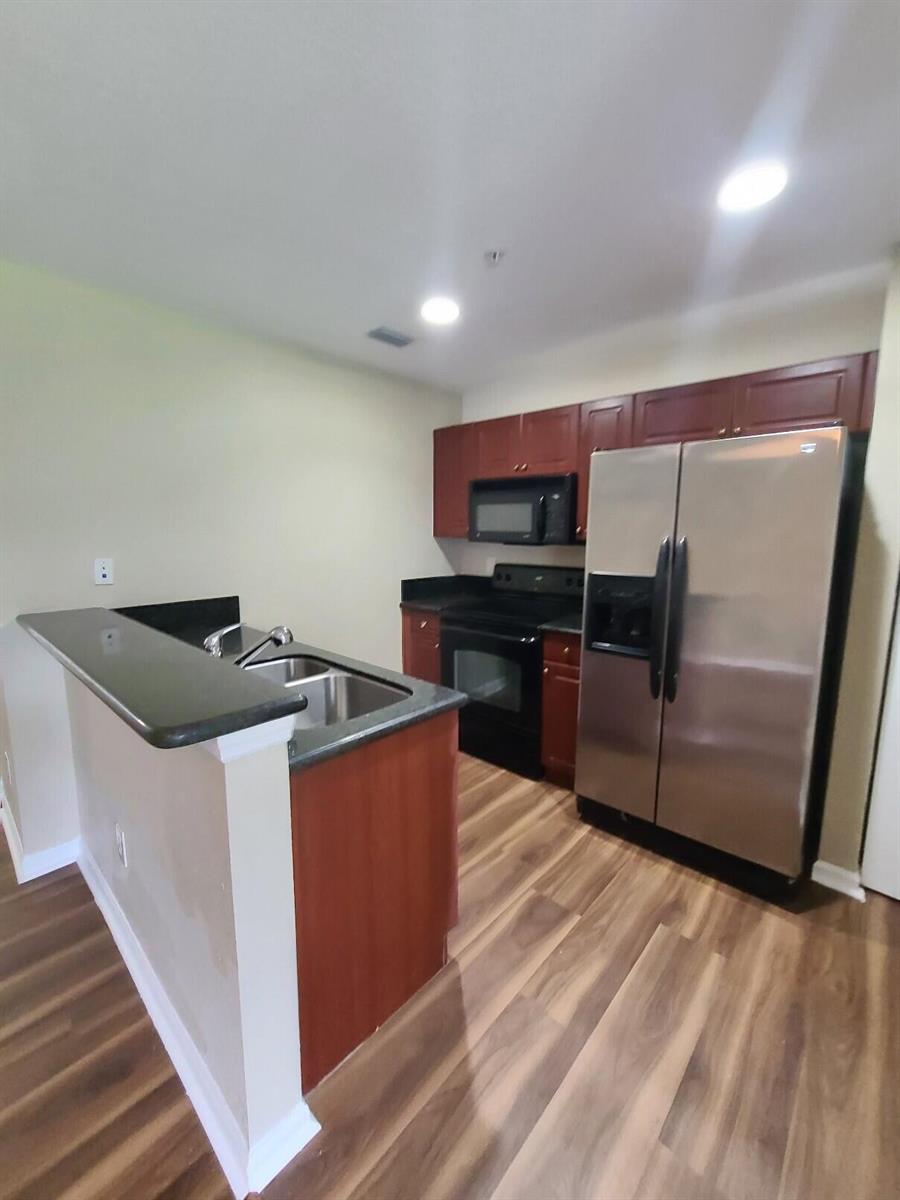 A kitchen features dark wood cabinets, black countertops, stainless steel appliances, and wood-look flooring — 1955 Freeport Drive, Riviera Beach FL 33404, RIVIERA BEACH, FL