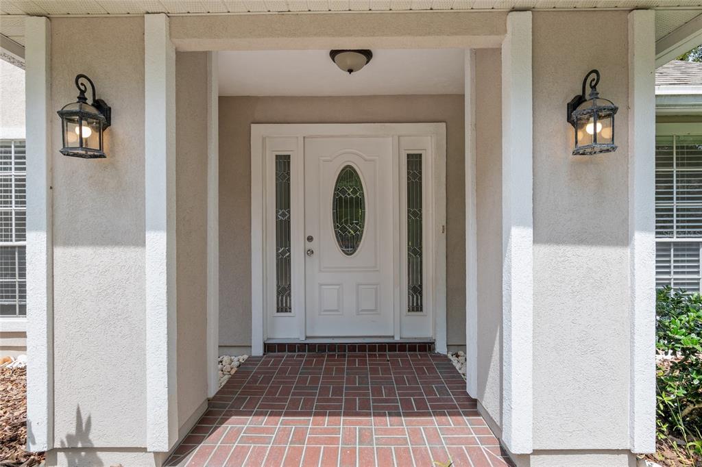 A white front door with a glass oval insert sits under a covered brick entryway — 10021 SW 42ND ROAD, GAINESVILLE, FL