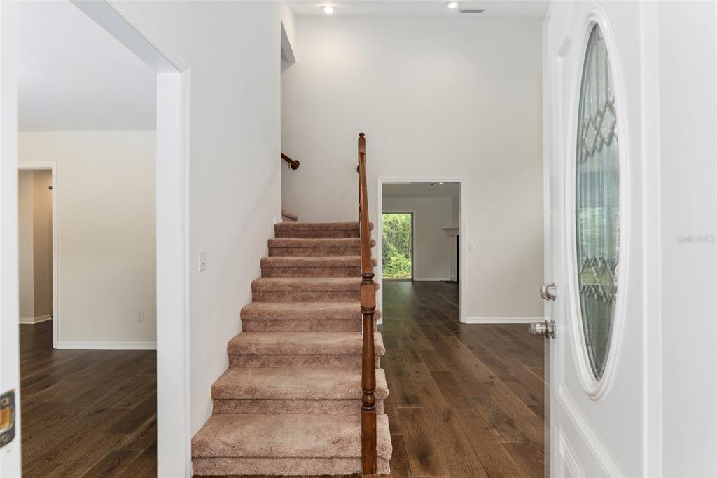 An entryway features a carpeted staircase, wood-look flooring, and a white front door with glass — 10021 SW 42ND ROAD, GAINESVILLE, FL