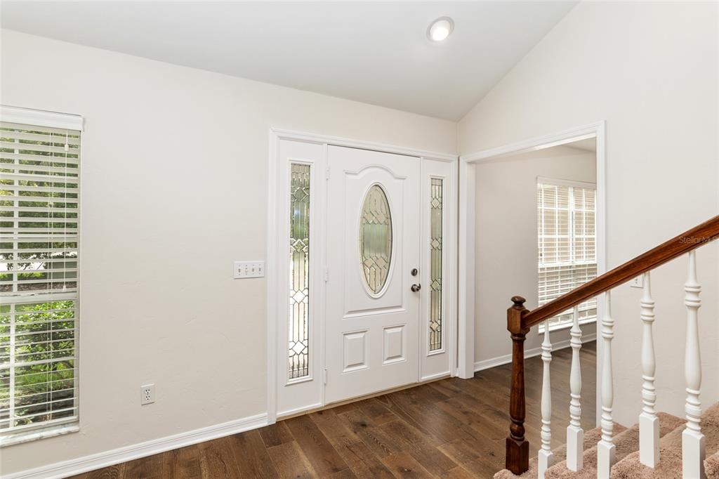 An entryway with a white front door, sidelights, hardwood floors, and a carpeted staircase — 10021 SW 42ND ROAD, GAINESVILLE, FL