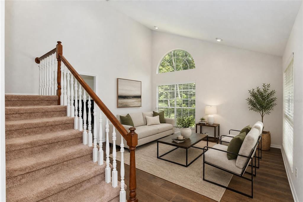 A living room features a carpeted staircase, vaulted ceilings, and neutral furniture on wood flooring — 10021 SW 42ND ROAD, GAINESVILLE, FL